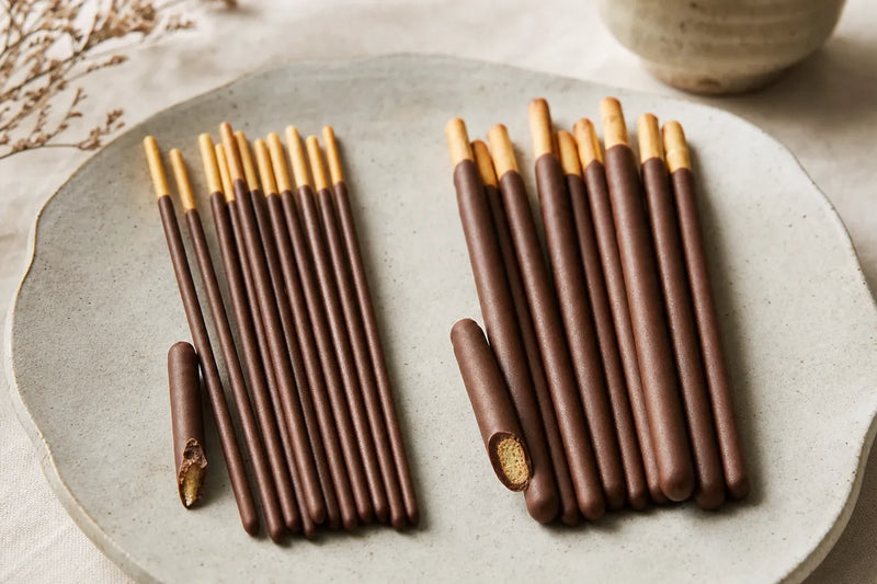 Részben bevont Pocky- és Pepero-jellegű kekszpálcikák egymás mellett, látható kekszmaggal és fogórésszel